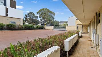 A parking area with a building on the left, a fenced area, and vegetation in the foreground.