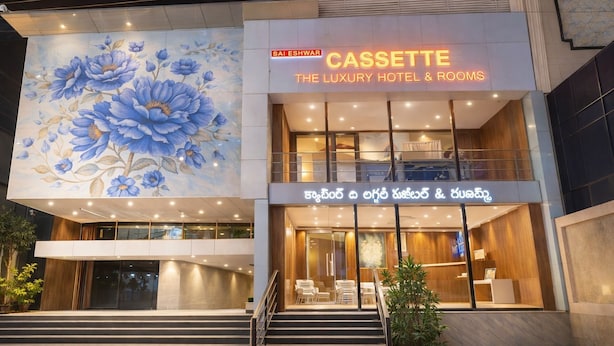 Un hôtel orné d’une grande fresque florale, avec une enseigne indiquant « CASSETTE, HÔTEL DE LUXE ET CHAMBRES », et un escalier menant à l’entrée.