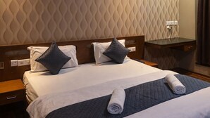 Une chambre d’hôtel avec un grand lit, une tête de lit en bois, une table de chevet et un bureau avec une chaise.