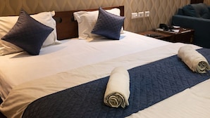 Un lit bien fait, recouvert d’une courtepointe matelassée, avec deux oreillers et deux serviettes enroulées, posés sur un plancher en bois.
