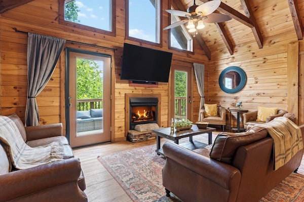 Cozy cabin living with vaulted wood ceilings, a fireplace, and direct deck access for relaxing mountain downtime.