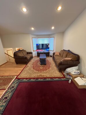 Ein Wohnzimmer mit zwei Sofas, einem Couchtisch, einem Fernseher und einem gemusterten Teppich.