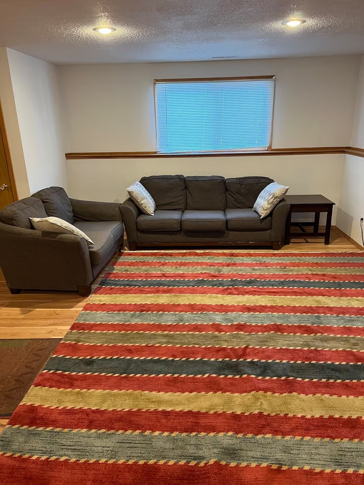 Uma sala de estar com sofá, uma poltrona, uma mesinha e um tapete listrado.