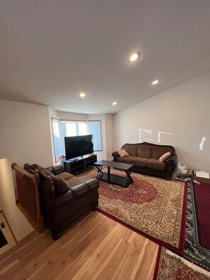 Ein Wohnzimmer mit einem braunen Ledersofa, einem Couchtisch aus Holz, einem Fernseher und einem gemusterten Teppich.