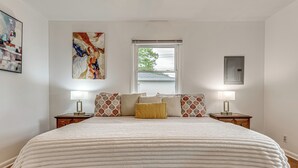 Ein Schlafzimmer mit einem großen Bett, zwei Nachttischen, einem Fenster mit Jalousien und einer wandmontierten Steckdose.