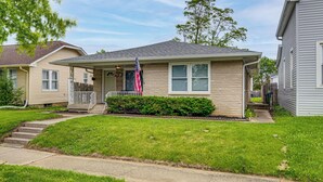 Ein eingeschossiges Haus mit Veranda, kleinem Vorgarten und deutlich sichtbarer amerikanischer Flagge.
