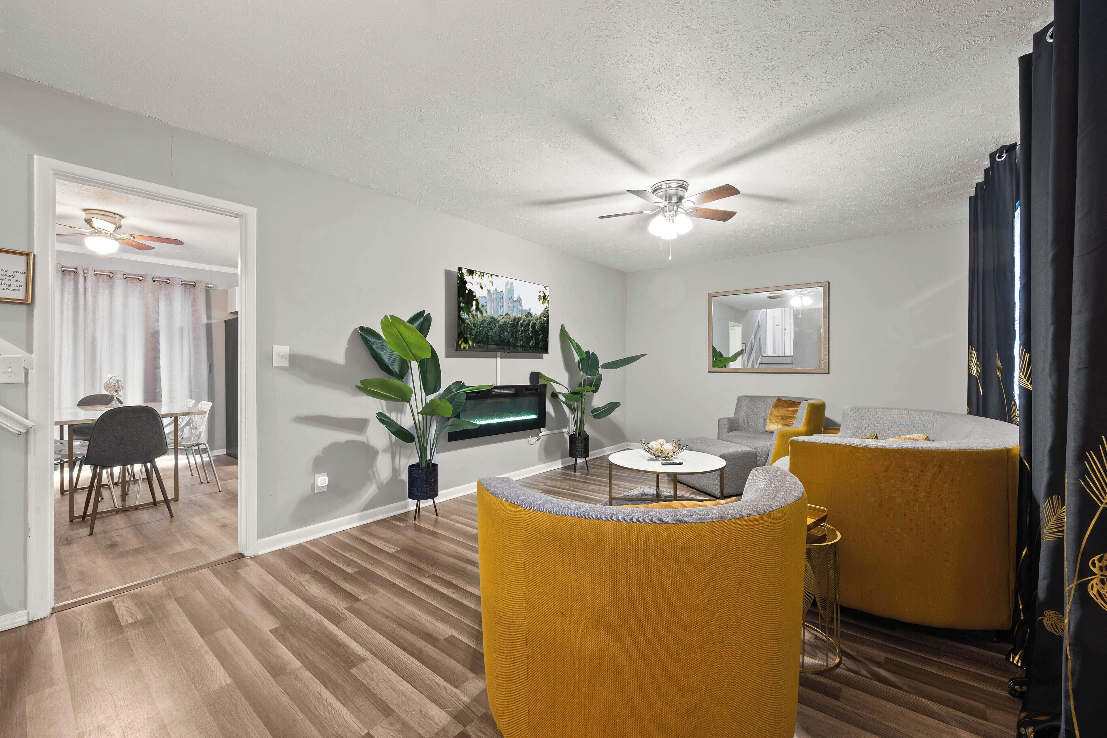A living room with a ceiling fan, a flat-screen TV, a sofa, a coffee table, and a dining area with chairs and a table.