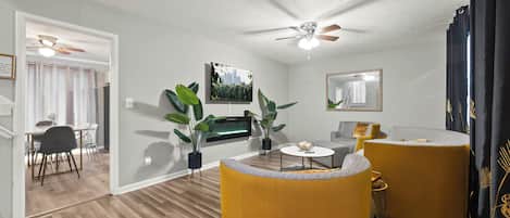 Una sala de estar con ventilador de techo, televisor de pantalla plana, sofá, mesa de centro y un comedor con sillas y una mesa.