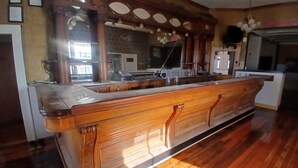 A bar area with a wooden counter, a large mirror, and a ceiling fan. - Five Mile Hotel - America's Most Famous Roadhouse (Butte)