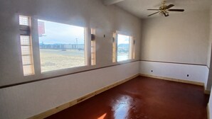 A room with a red floor, large windows, and a ceiling fan. - Five Mile Hotel - America's Most Famous Roadhouse (Butte)