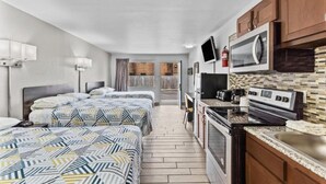 A compact hotel room with two beds, a kitchenette, a flat-screen TV, and a view of the street.