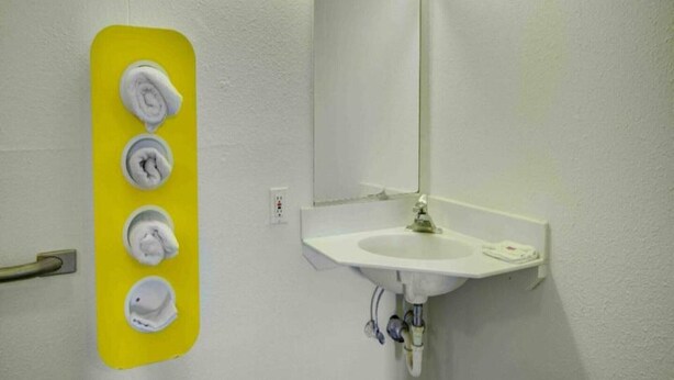 A bathroom with a white sink, a mirror, and a yellow towel dispenser with four towels.