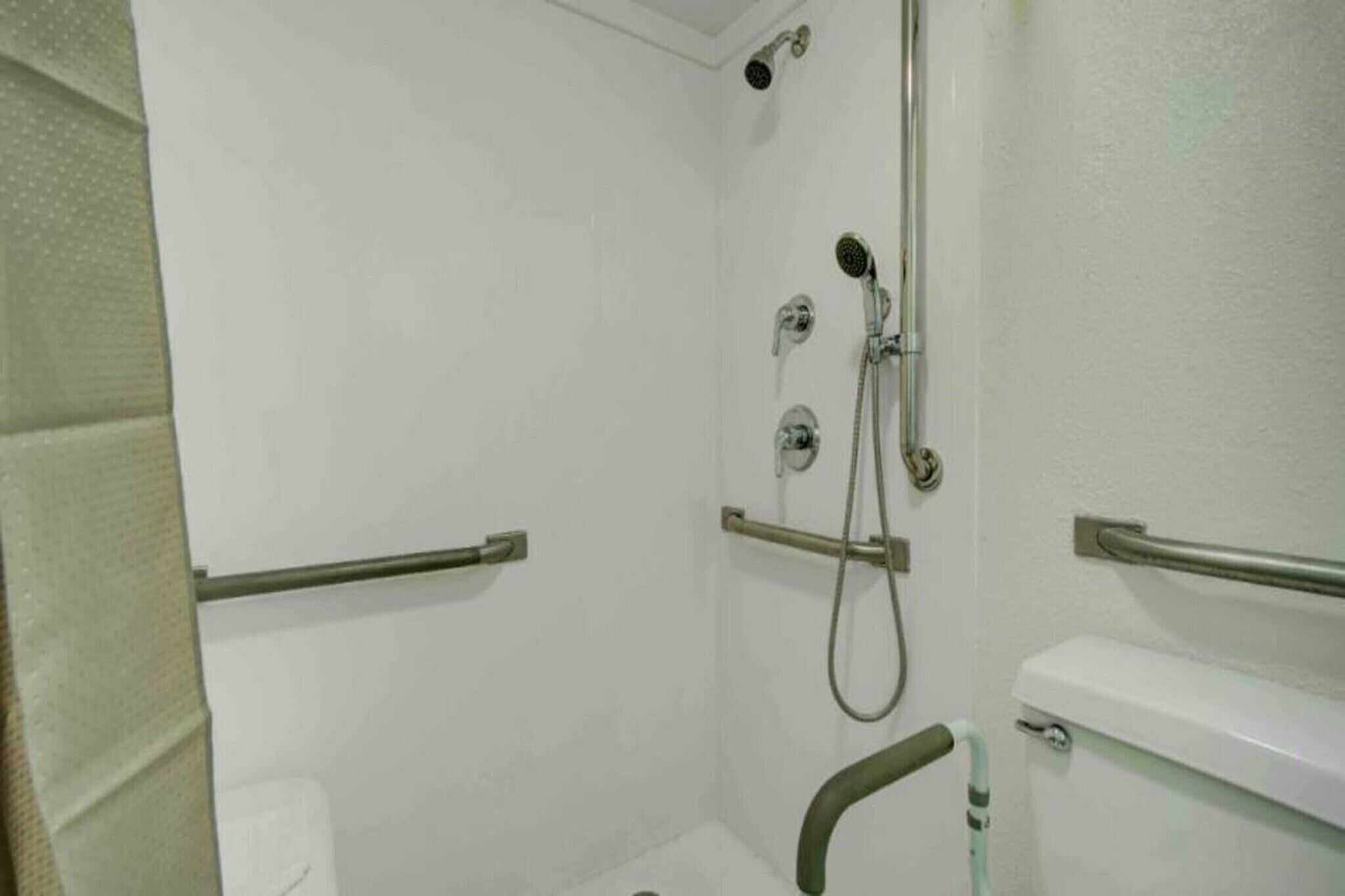 A bathroom with a shower, toilet, and grab bars.