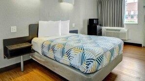 Een hotelkamer met een bed, nachtkastje, airconditioning en een raam met gordijnen.