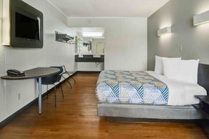 A hotel room with a bed, a desk, a chair, a TV, and a mirror.