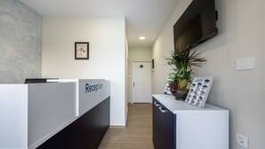 A reception area with a reception desk, a potted plant, a framed picture on the wall, and a door in the background. - SolMare Premium Suite (Mastihari)