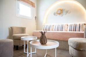 Ein gemütliches Zimmer mit einem Bett, zwei weißen runden Tischen, einem gewebten Korb und einem Fenster mit Vorhang.