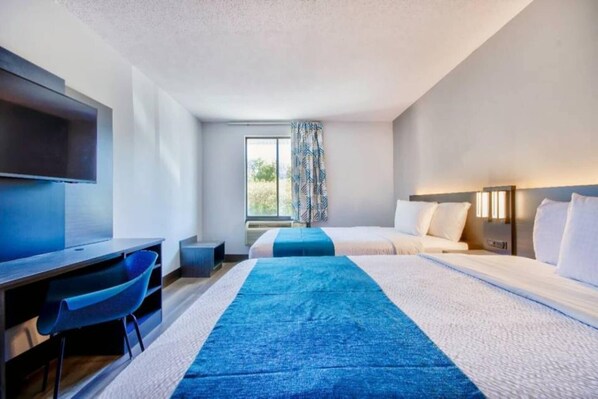 A hotel room with a desk, two beds, a TV, and a window with curtains.