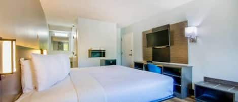 Una habitación de hotel con cama, escritorio, televisor y espejo.