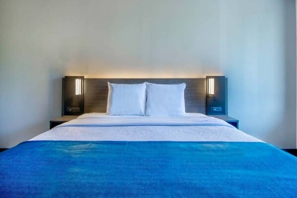 A hotel room with a bed, two bedside lamps, and a blue blanket.