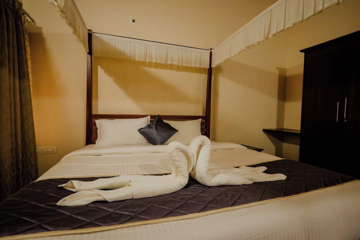 Una cama con dosel, con un edredón oscuro, una colcha blanca y una sola almohada oscura.