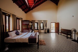 A room with a bed, a bench, a fan, and a door leading to another room. - Akruthi Palm Pavilion Resort (Chikkamagaluru)