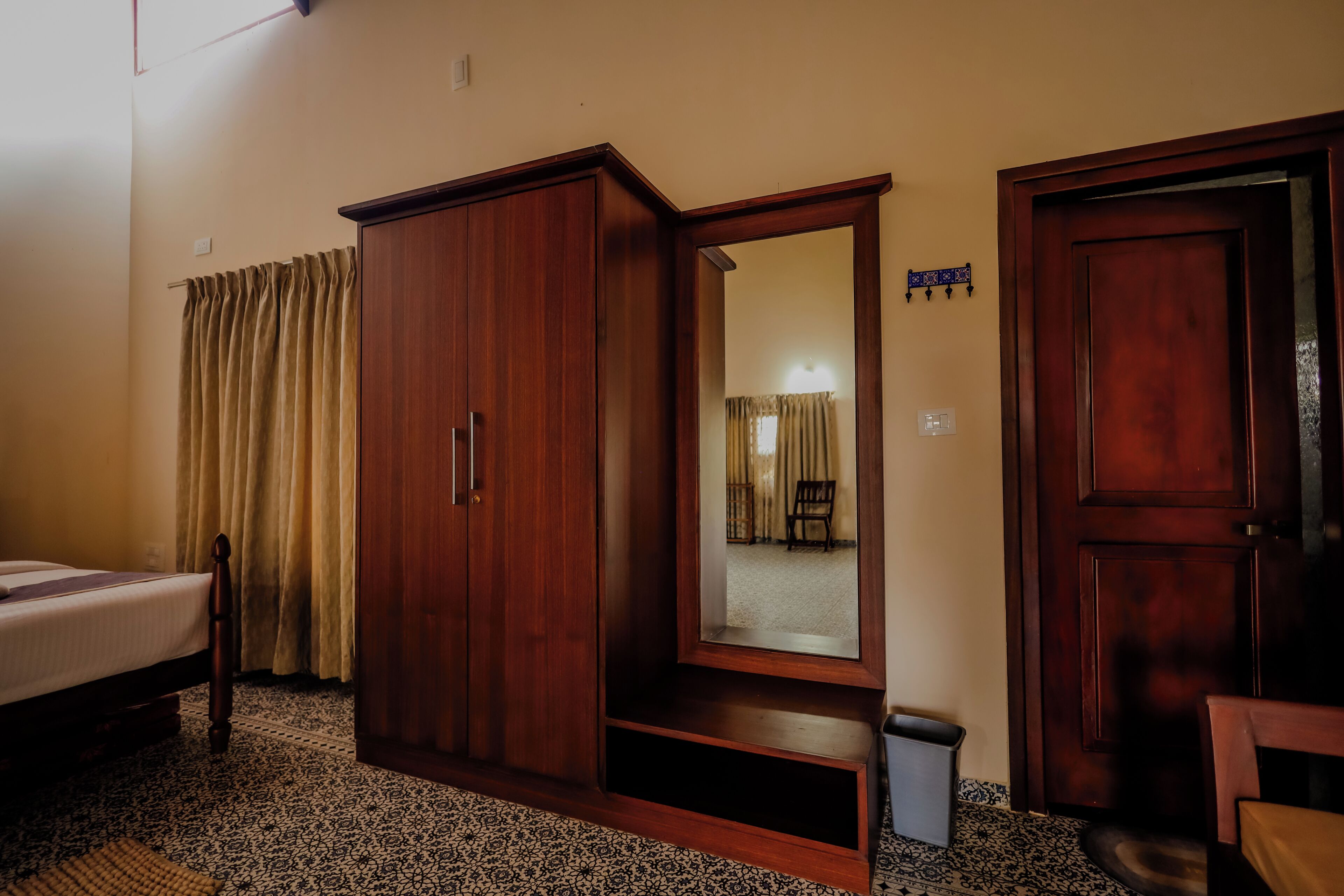 A hotel room with a bed, a wardrobe, a mirror, a door, and a small trash bin.