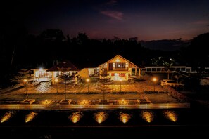 A two-story house with a balcony, a driveway, and a well-lit front yard. - Akruthi Palm Pavilion Resort (Chikkamagaluru)
