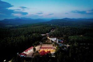 An aerial view of a property with a large building, a parking area, and surrounding forested hills. - Akruthi Palm Pavilion Resort (Chikkamagaluru)