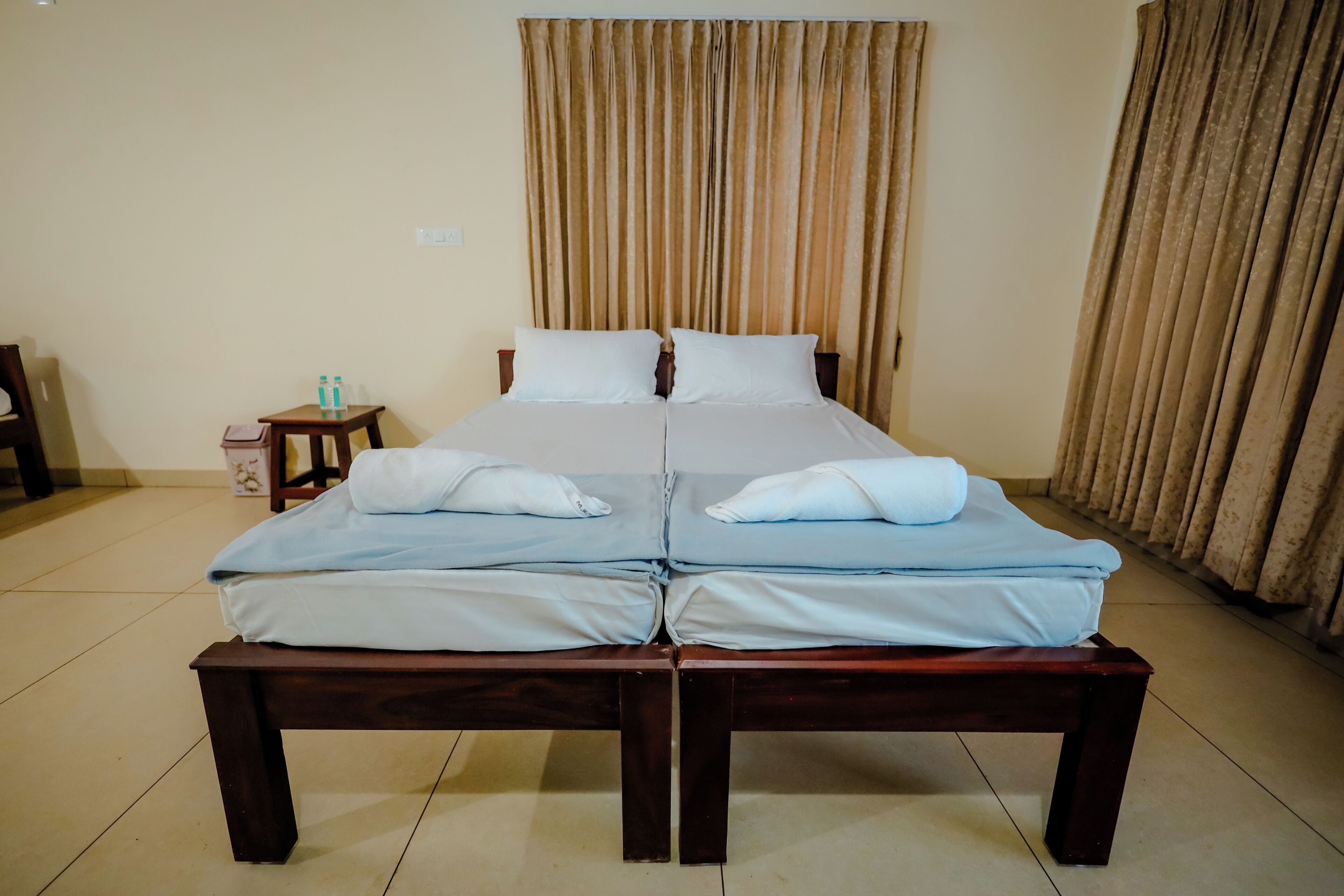 Una cama doble con dos almohadas, una mesita de noche con botellas de agua y una cortina.