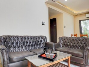 Ein modernes Wohnzimmer mit einem gepolsterten Ledersofa, einem Glastisch und einem kleinen Beistelltisch mit einer Kaffeetasse und einem Wasserkocher.