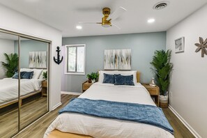 Ein Schlafzimmer mit Bett, Deckenventilator, großem Spiegel und Fenster mit Jalousien.