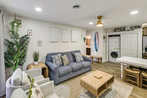 Ein Wohnzimmer mit grauem Sofa, Holztisch und einer großen Pflanze.