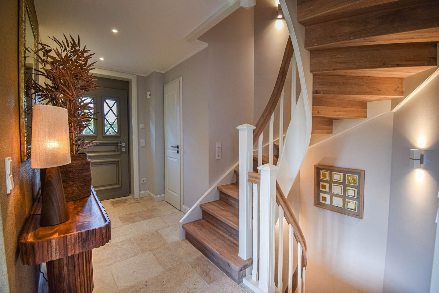Een modern interieur met een houten trap, een deur met raam en een wandlamp.