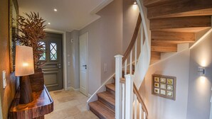 Un intérieur moderne avec un escalier en bois, une porte dotée d’une fenêtre et un luminaire fixé au mur.