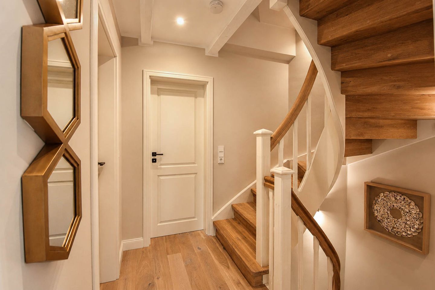 A staircase with wooden steps and white railings, a white door, and a wall-mounted mirror.