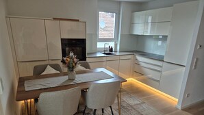 A modern kitchen with a dining area, featuring a wooden table, two chairs, and a rug. - Premium Lake Constance Base Apartment – Modern, Cozy & Well-Maintained (Rielasingen-Worblingen)