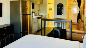 Una habitación de hotel compacta con cama, una mesita, una silla, kitchenette y un sofá.