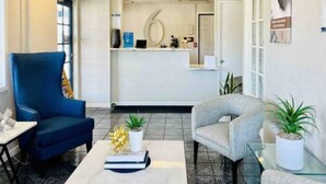 Zona de recepción con un escritorio, una silla azul, una silla gris y una mesa de centro con un libro y una planta.
