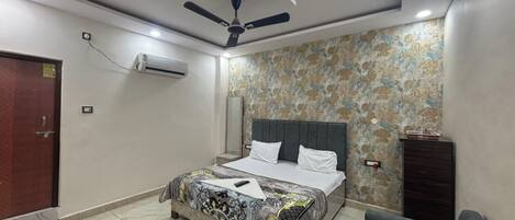 A bedroom with a bed, a ceiling fan, an air conditioning unit, a patterned wall, and a dark-colored dresser.