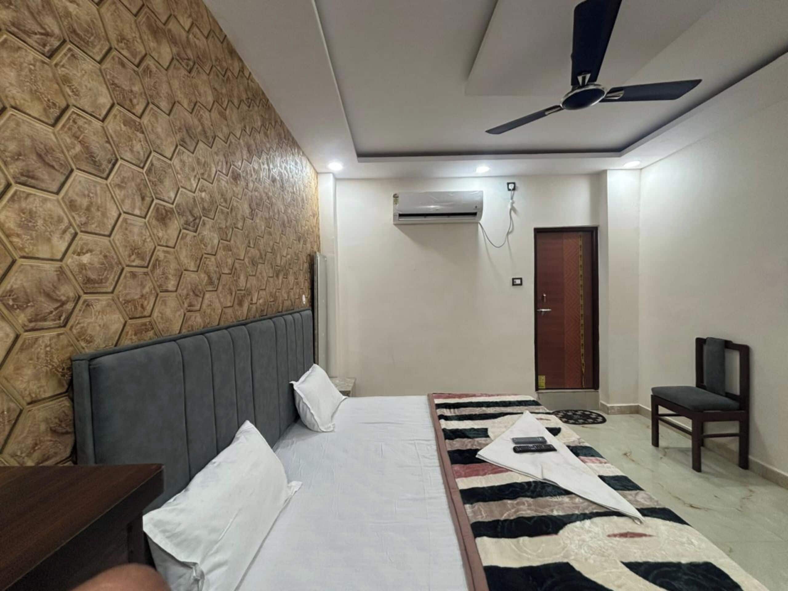 A bedroom with a bed, a headboard, a ceiling fan, an air conditioning unit, a door, and a chair.