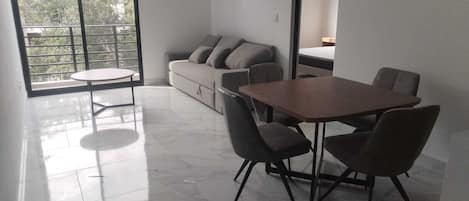 A modern room with a dining table, chairs, a sofa, and a balcony with a railing.