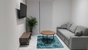 Ett modernt vardagsrum med en soffa, ett soffbord, en tv som är monterad på väggen och en krukväxt.