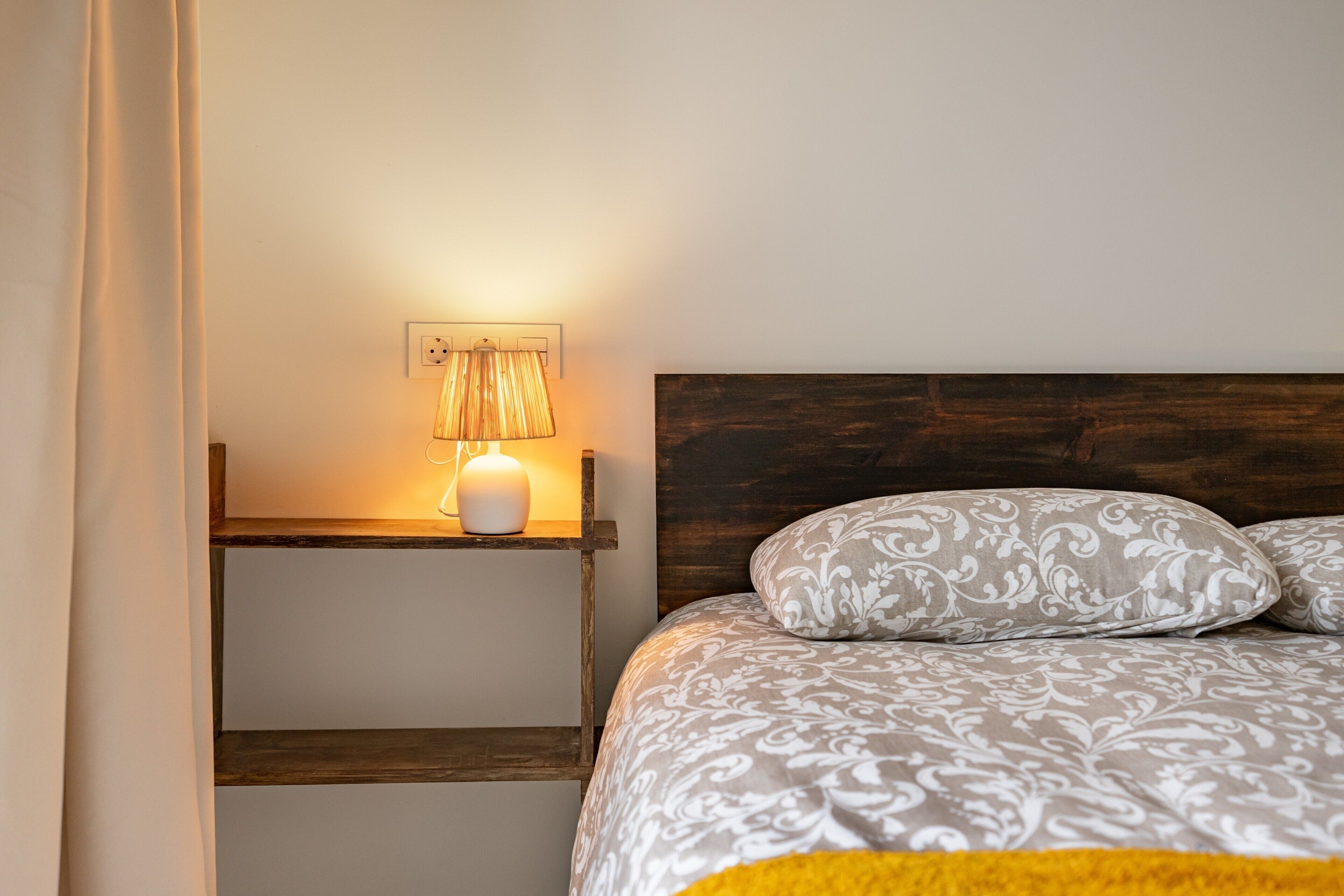 Een slaapkamer met een bed, een bedlampje, een nachtkastje en een stopcontact.