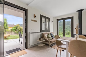 Habitación con sofá, una mesa y una silla. Se ve vegetación a través de la ventana.