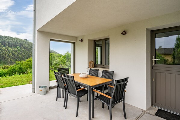 An outdoor patio with a table and chairs, a door, and a view of a green landscape. - Apartment 'Tierra' with Sea Views, Private Terrace and Wi-Fi (La Vega)