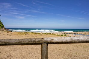 Una playa con valla de madera, costa rocosa y olas del océano.