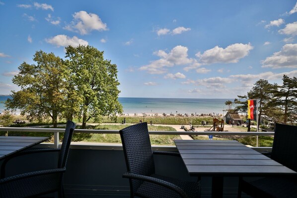 A beach view from an outdoor seating area with tables and chairs, a flag, and a tree. - Strandkoje 203 - Holiday apartment Scharbeutz directly on the beach - Strandkoje 203 for (Scharbeutz)