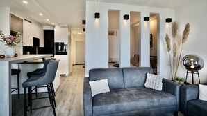 A modern living area with a grey sofa, bar stools, and a kitchen in the background. - Strandkoje 203 - Holiday apartment Scharbeutz directly on the beach - Strandkoje 203 for (Scharbeutz)
