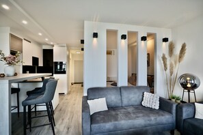 A modern living area with a grey sofa, bar stools, and a kitchen in the background. - Strandkoje 203 - Holiday apartment Scharbeutz directly on the beach - Strandkoje 203 for (Scharbeutz)